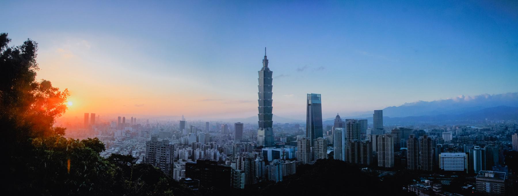 Wide panorama of the Taipei skyline at sunset, tower silhouettes against an amber sky