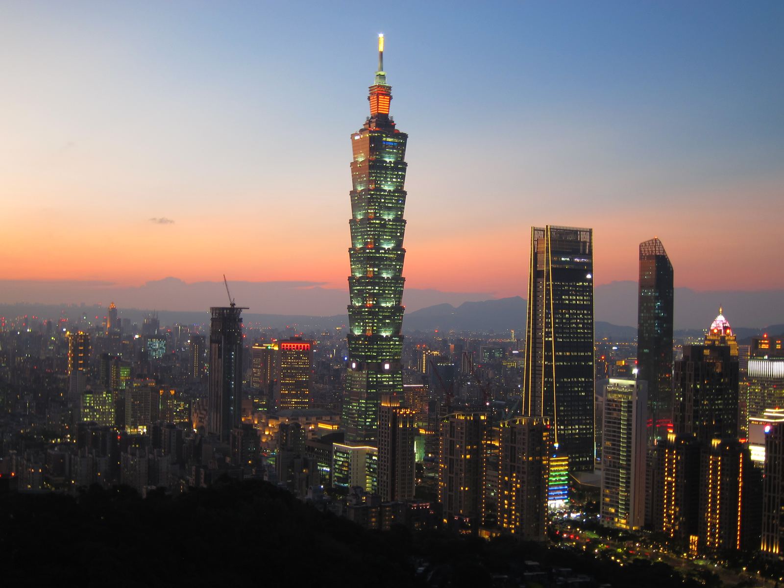 Taipei skyline at deep twilight, city lights beginning to glow under a dark blue sky